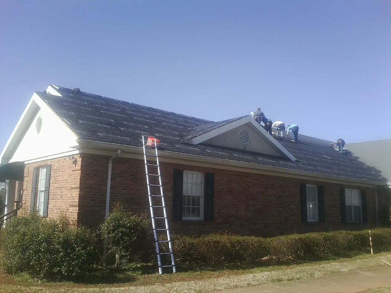 Crew tearing shingles off a brick ranch roof with a ladder set — Emergency Roof Repair work by our crew in Glen