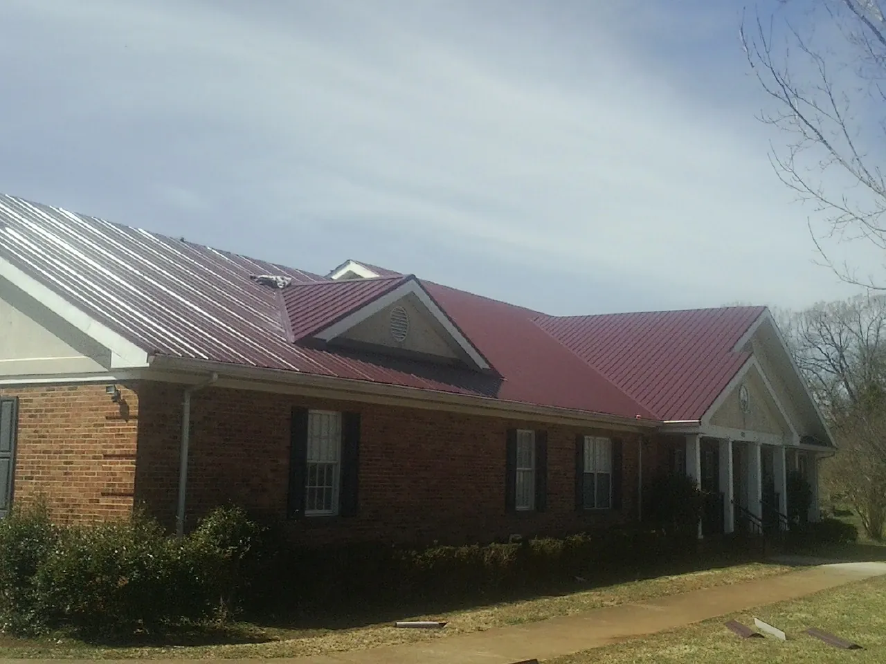 Red metal roof with gabled entries on a long brick building, from a Hail Damage Roof Repair job in Glen